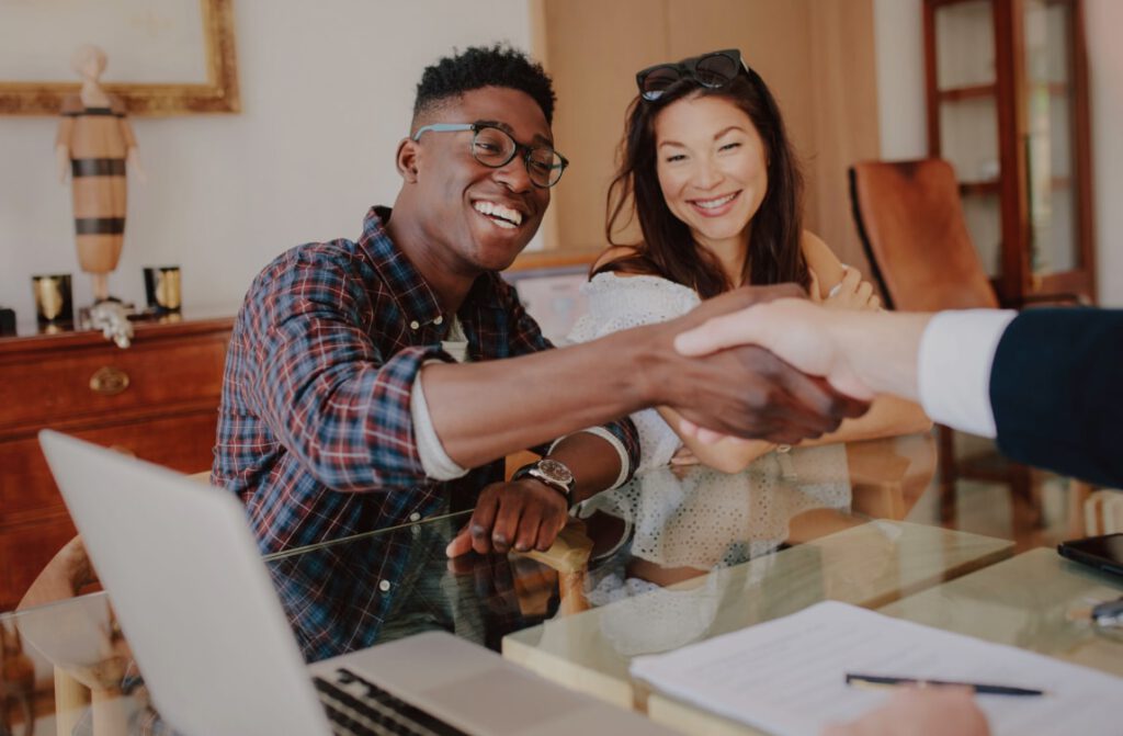 Smiling couple shaking hands with a loan officer, symbolizing a successful closing process.